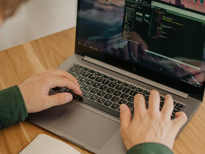 Hands typing on a laptop next to an open notebook and pen.