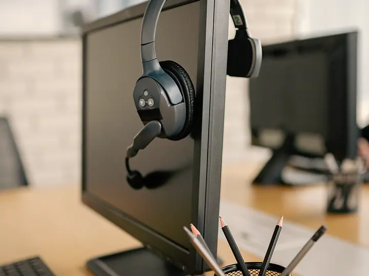 A headset resting on top of a monitor at a tidy desk.