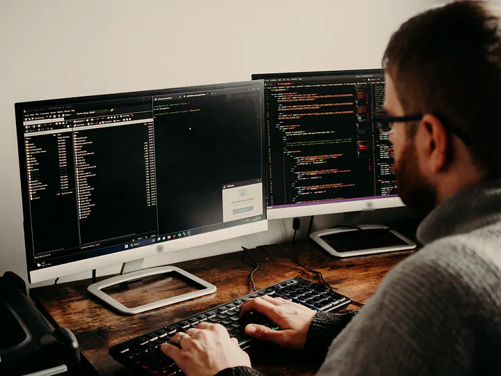 A developer typing at a desk with two monitors of code and a terminal.